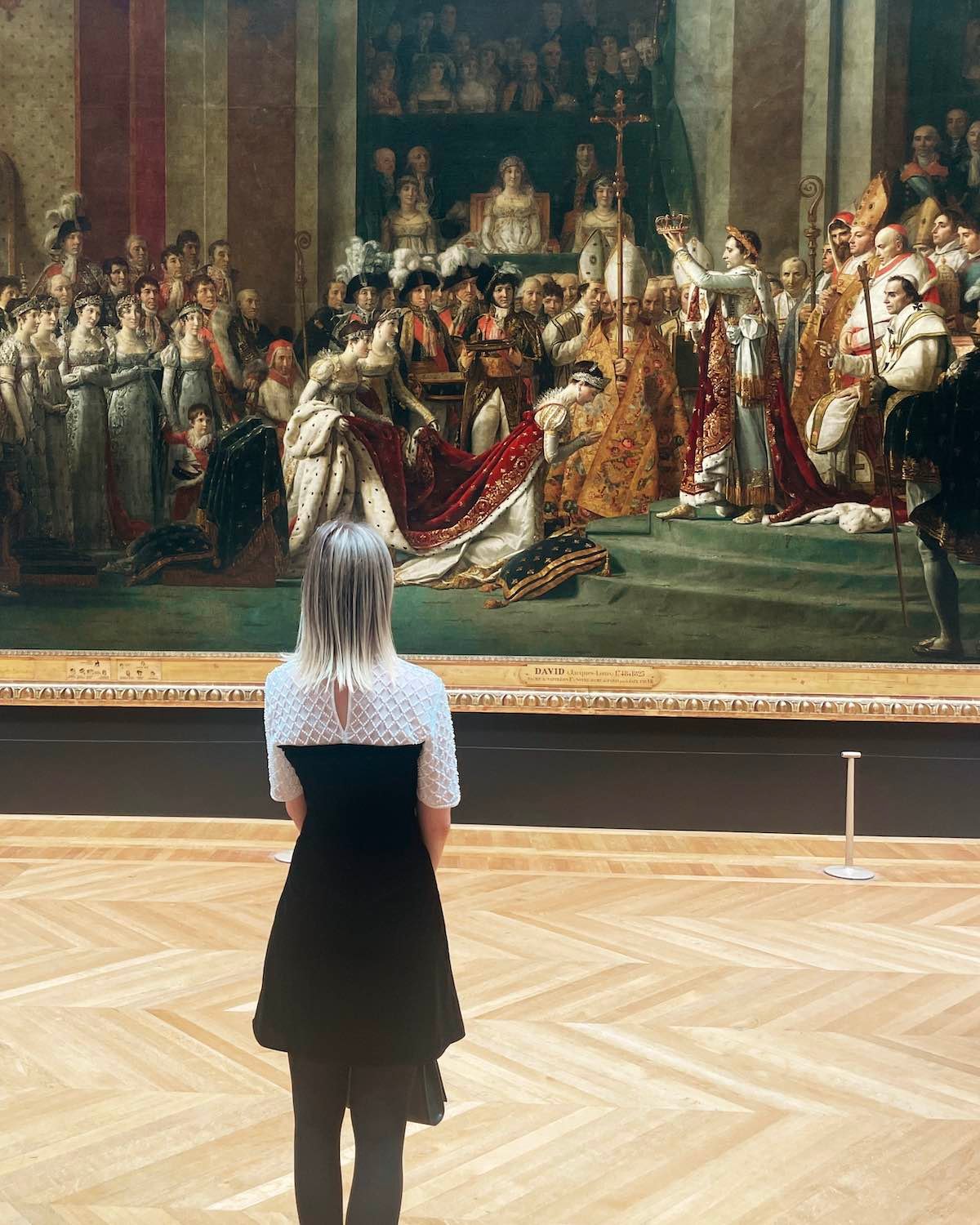 woman in a dress standing in the Louvre museum in front of a historic painting